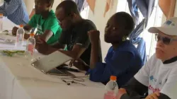 Masapi (en t-shirt blanc) et d'autres personnes suivant le déroulement de la réunion. / 